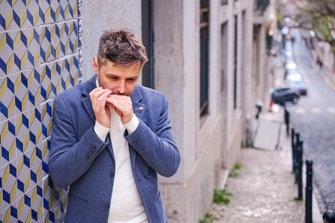Man musician in a blue blazer and white sweater playing blues on a harmonica with eyes closed,