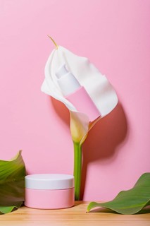 Elegant cosmetic jar alongside a vibrant calla lily on a pink background, suggesting luxury and