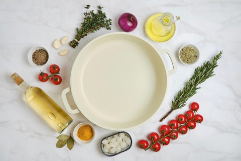 Fresh vegetables, herbs, white wine and cooking oil are arranged on a kitchen countertop next to an