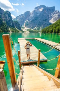 Woman standing on wooden pier, admiring stunning landscape of lake braies with emerald waters and