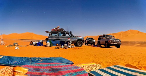Off-roaders and camping equipment in the middle of a vast desert landscape under a blue sky, with