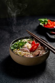A steaming bowl of Vietnamese Beef Pho Noodle Soup (Pho Bo), garnished with slices of beef, fresh