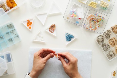 Top view of cropped unrecognizable hands of a woman creating jewelry in her studio. Surrounded by