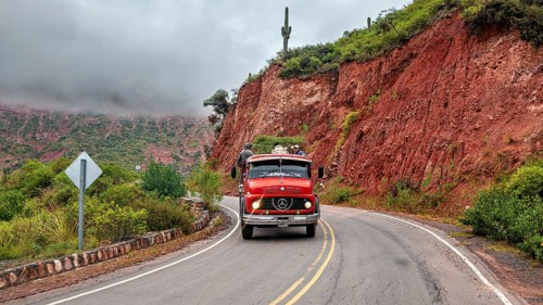 Red bus travels on a winding road along a red mountain face, roads through the countryside of the