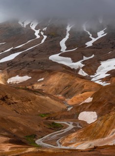 Stream between colourful rhyolite mountains with snowfields, Hveradalir geothermal area,
