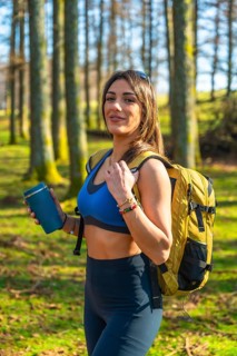Young hiker woman walking in a forest holding a reusable coffee cup, wearing sportswear and
