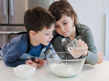 Two young siblings engage in a baking activity, attentively measuring and mixing ingredients in a