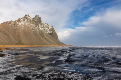 Teared water on lava sandy beach against mountain backdrop, sea, snow, winter, Stokksnes,