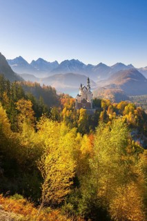 Neuschwanstein Castle in an autumnal landscape with mountains and glowing trees, Schwangau,