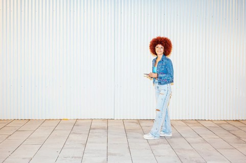 African descendent woman with vibrant afro hair, wearing a denim jacket and ripped jeans, stands