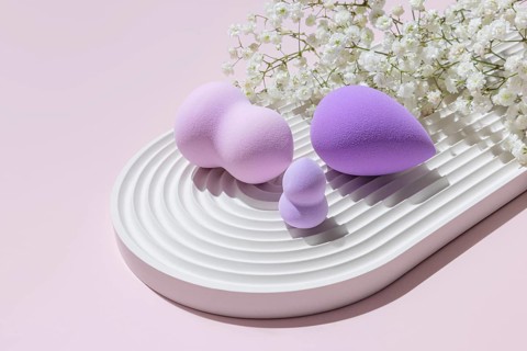 Various sizes and shapes of purple-toned makeup sponges expertly staged on a white ridged tray,