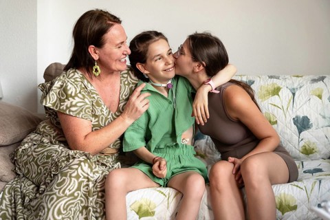 A family shares a joyful moment on the couch. The young daughter, wearing a tracheostomy tube,