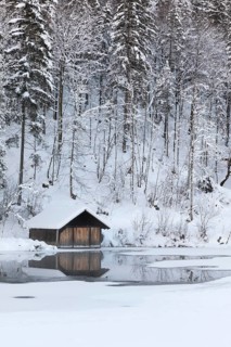 Snow covered boat shelter on Lake Almsee which is partly frozen and snow covered. Snow on the