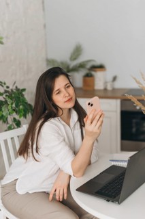 A nutritionist sits at a white desk, engaging in an online consultation via smartphone. A laptop