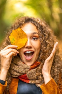 Vertical portrait of a playful woman hiding among yellow leaf