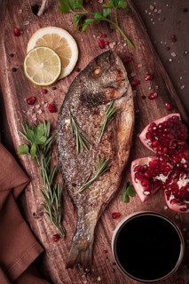 Fried dorado fish, with spices and herbs, on a wooden board, pomegranate sauce, close-up, no people