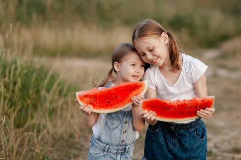Two joyful children savor large slices of watermelon outdoors during a bright summer day. Their