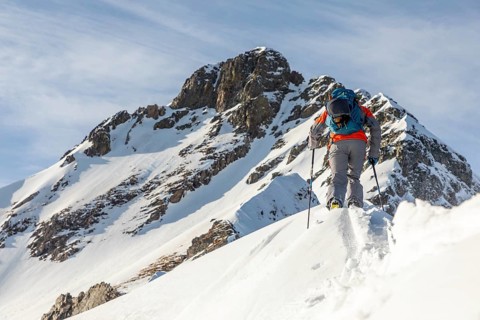 A ski tourer ascends a snow-covered mountain, showcasing determination and adventure. The bright