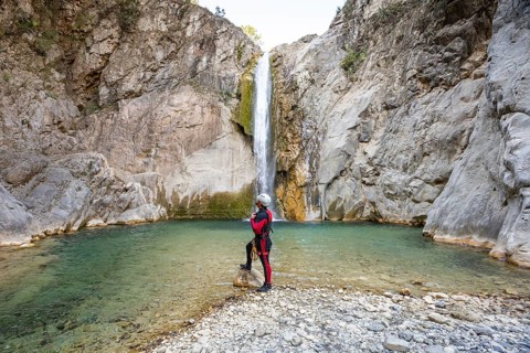 Man in canyoneering gear gazes at a waterfall in Matacanes, Nuevo Leon, Mexico. She stands on a