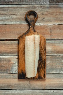 A clean, freshly sliced fillet of white fish rests on a handcrafted wooden cutting board