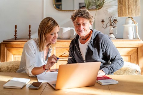 A couple engaged in work at home, sitting at a wooden table with a laptop and documents The room