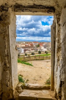 Crumbling walls of ancient caves frame a view of arguedas village in navarre, spain, under a partly
