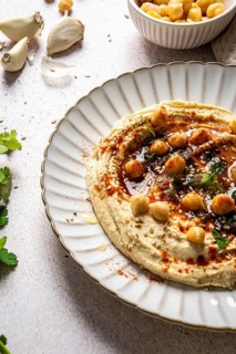 Creamy hummus served on a white plate, garnished with whole chickpeas, paprika, olive oil, and