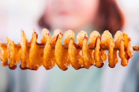 Close-up of golden spiral tornado potatoes on a stick, drizzled with sauce. This tasty snack is