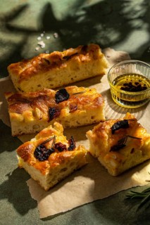 Slices of golden homemade focaccia topped with rosemary and dried tomatoes, paired with olive oil