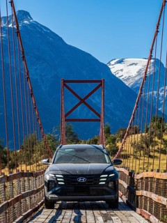SUV driving over old-style orange suspension bridge, river Rio Nadis south of Cochrane, mountain