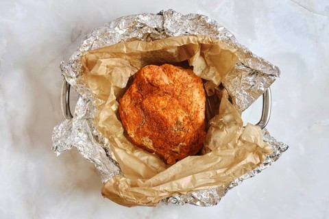 An oven roasted pork shoulder is resting in a pan with unwrapped parchment paper and foil. This