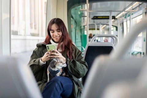 A young woman with a smartphone and a small chihuahua sits in a modern tram, enjoying a comfortable