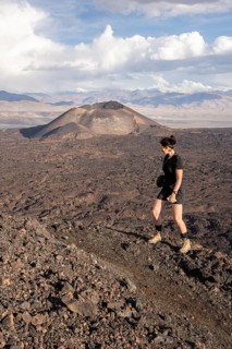 Woman on a hike through rocky terrain with volcano in the background, Argentina, volcanoes, lava
