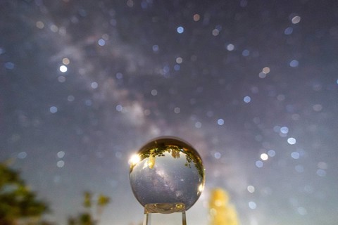An enchanting image capturing the Milky Way galaxy mirrored in a crystal ball, set against a blurry
