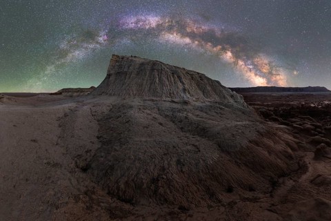 A stunning panoramic view of the Milky Way galaxy arched above a unique rock formation in Goblin