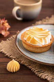 French lemon tart with meringue on brown wooden background, cup of coffee, linen textile, side