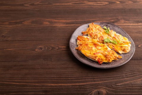 Baked chicken meat with cheese and tomatoes on brown wooden background. side view, copy space