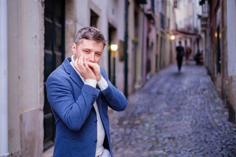 Man musician in a blue blazer and white sweater playing blues on a harmonica with eyes closed,
