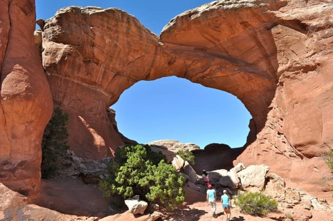 Group of hikers under a large rock arch, the Broken Arch, on a sunny day, Arches National Park,