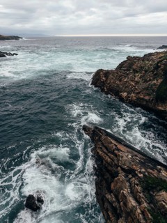 The image captures a dramatic coastal landscape with rocky cliffs and turbulent waves crashing