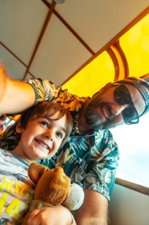 A man and a child are smiling at the camera. The man is wearing a green shirt with palm trees on it
