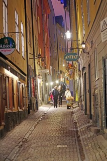 Narrow cobblestone alley at night, illuminated and lively with people, winter, Gamla Stan, Old