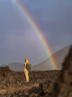 A woman with a backpack stands on volcanic terrain in Timanfaya National Park, Lanzarote, Spain,