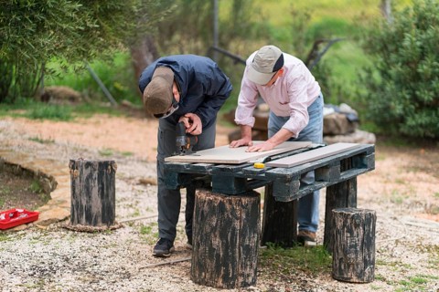 A senior father and his son bond while working on a carpentry project outdoors. Both are focused on