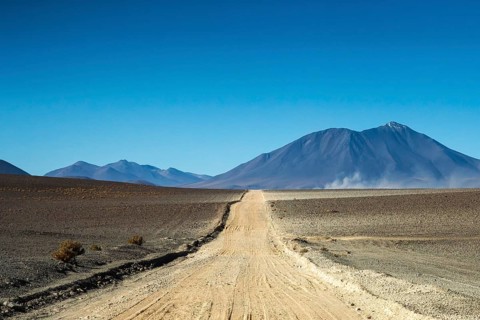 A vast gravel road meanders through the arid landscape of La Puna, Argentina, leading towards