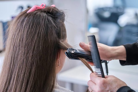 A hair stylist applies a flat iron to straighten a woman's hair in a beauty salon. The stylist