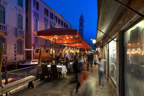 In the evening, lively restaurant on a canal with the tower of Santa Maria della Pietà in the back,