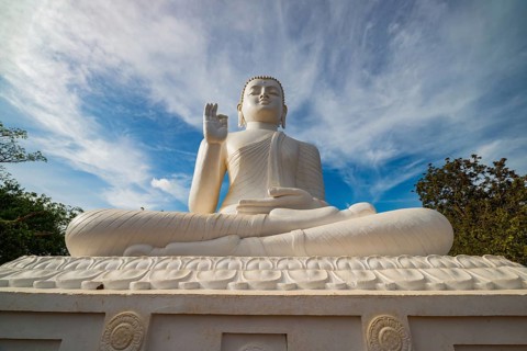 A stunning white Buddha statue in Sri Lanka, set under a vibrant blue sky with wispy clouds. This