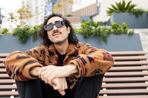 Stylish man with sunglasses and patterned jacket sits relaxed on a bench in an urban setting The
