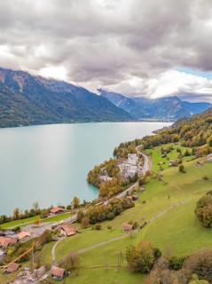 Alpine landscape with a lake, green meadows and hillside buildings under clouds, Lake Brienz.